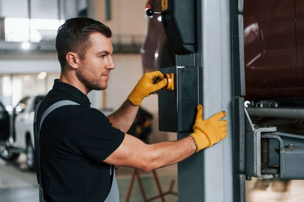 At daytime. Man in uniform is working in the auto service