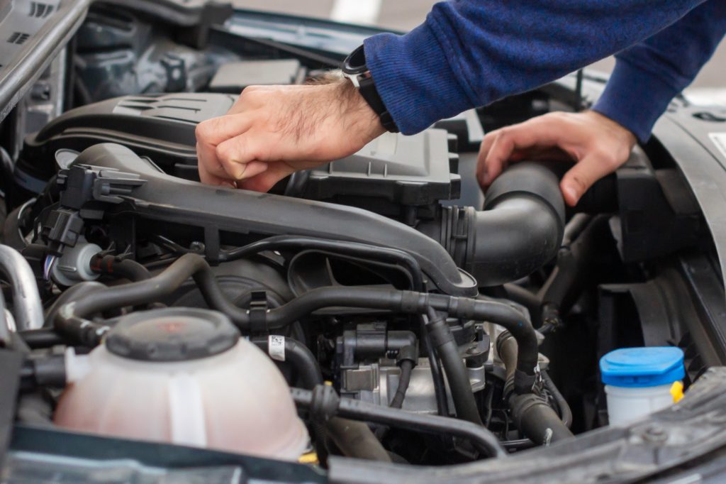 Closeup of mechanic hands checking motor under the hood in the broken car. Repairing of the vehicle