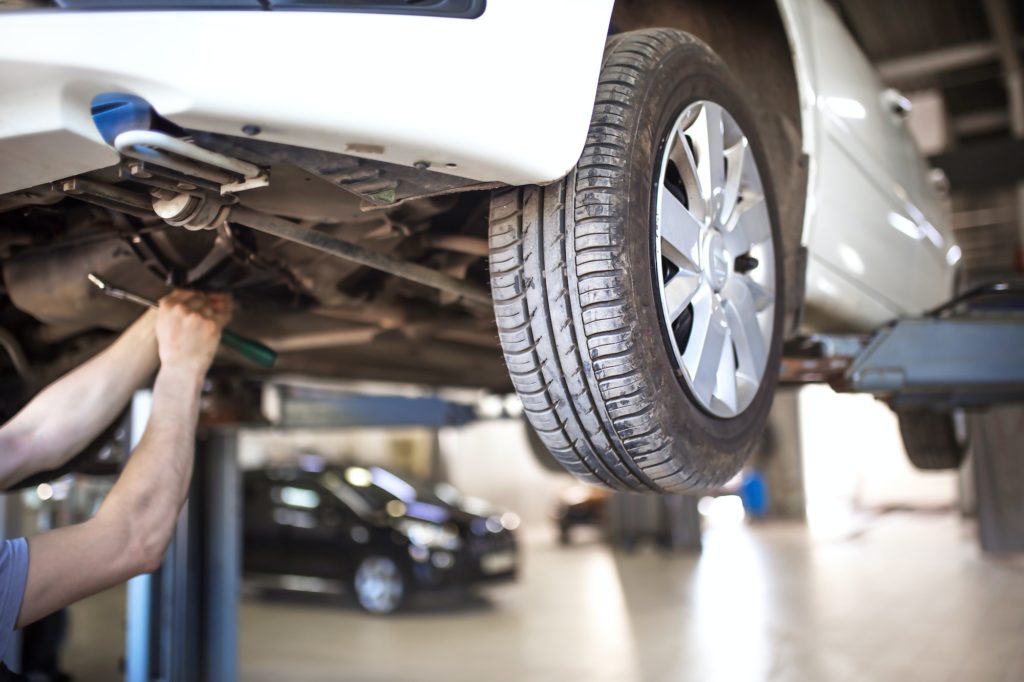 The car is lifted for repair on a lift in a car service station, a mechanic in overalls repairs